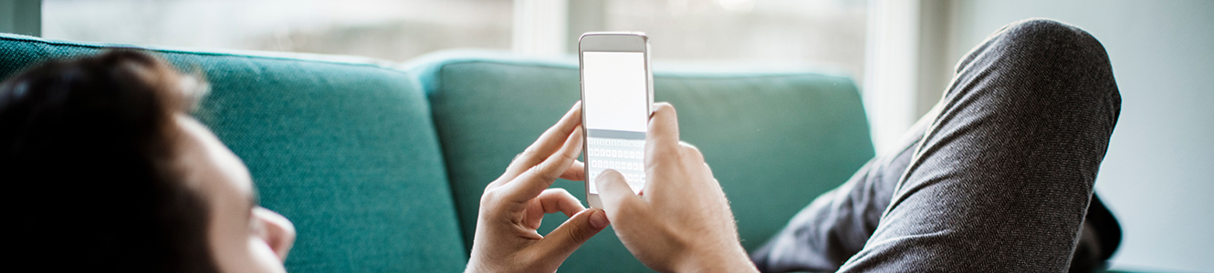 Man laying on couch looking at smart phone. 